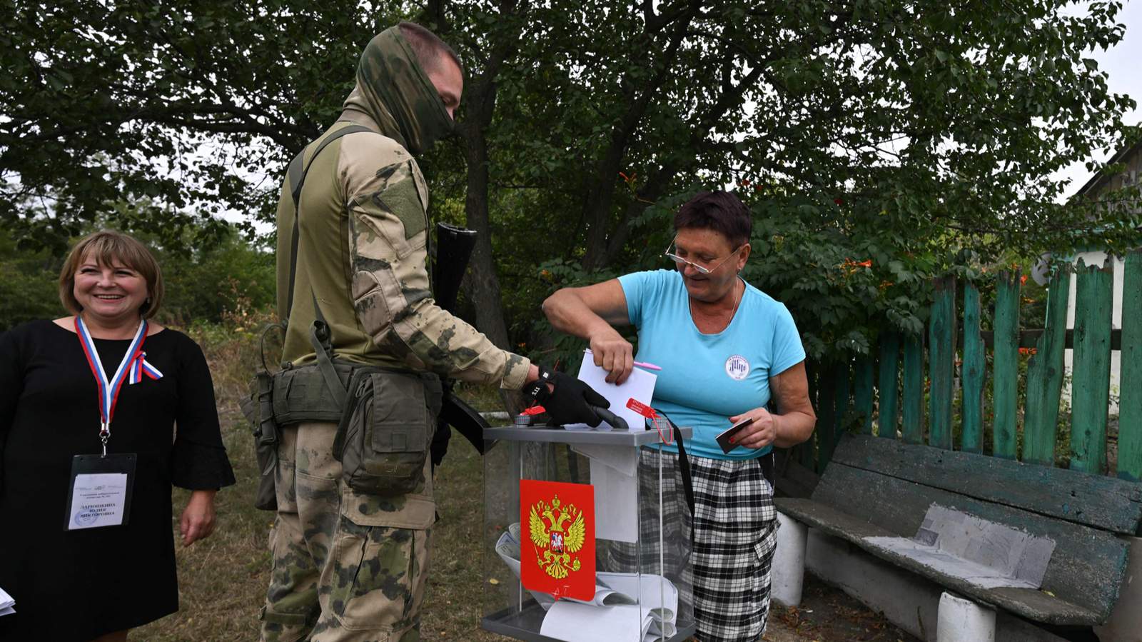 Женщина опускает бюллетень в переносную урну для голосования, которую держит российский военнослужащий, сопровождающий членов участковой избирательной комиссии во время надомного досрочного голосования на выборах в Госдуму РФ. Поселок Вербовка, Донецкая область, Украина. 14 сентября 2026 года. Фото: AFP / Scanpix / LETA