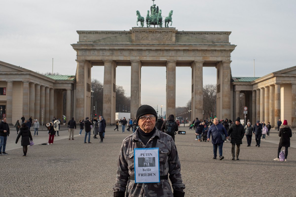 Мужчина с табличкой «Путин призывает к миру» на фоне Бранденбургских ворот, Берлин. Фото: Дмитрий Цыганов